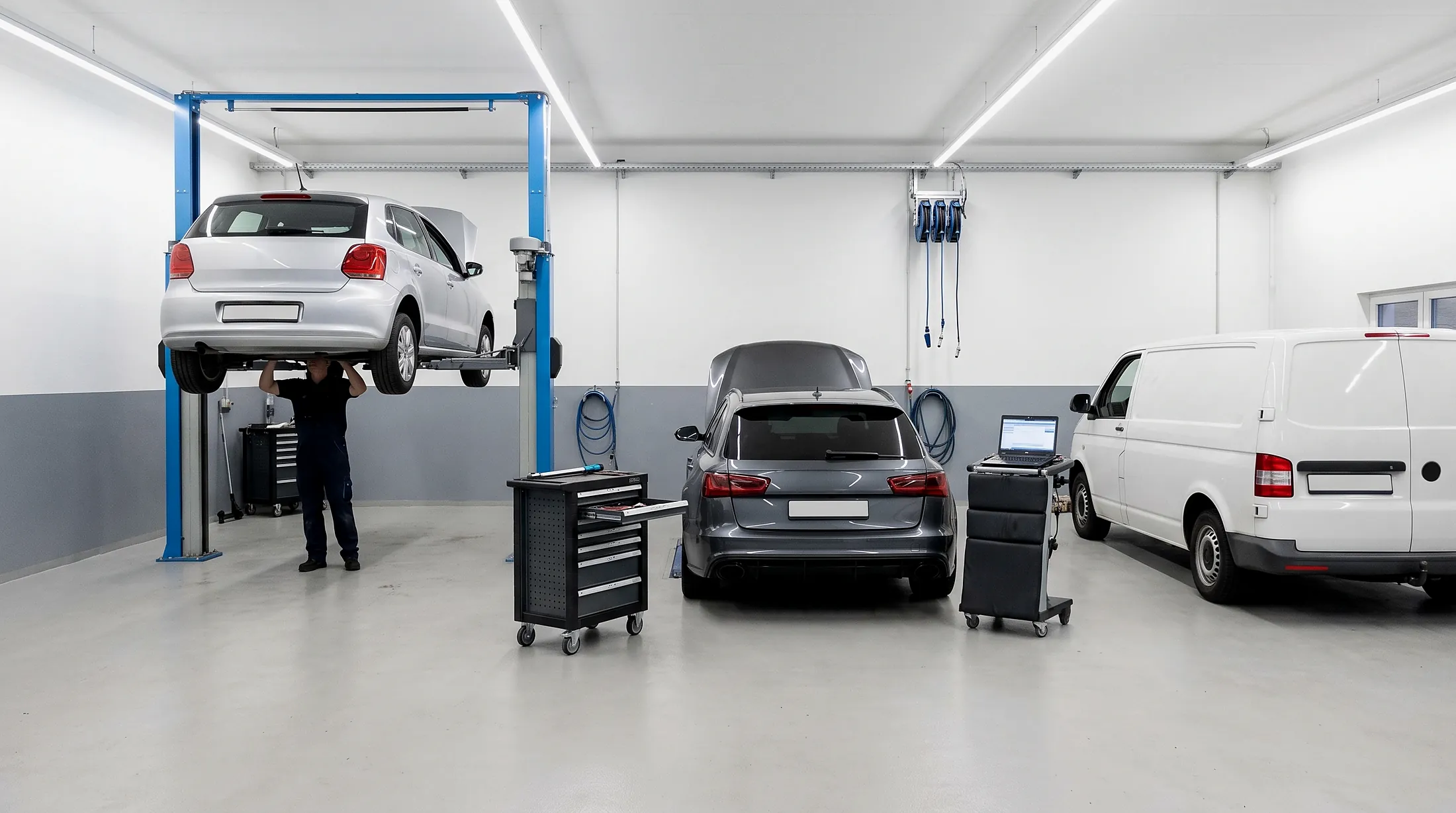 Werkstatthalle in Betrieb - HZ Performance Helle Werkstatthalle mit blauen Hebebühnen: ein Fahrzeug angehoben, ein Mechaniker darunter, daneben ein Kombi und ein Transporter