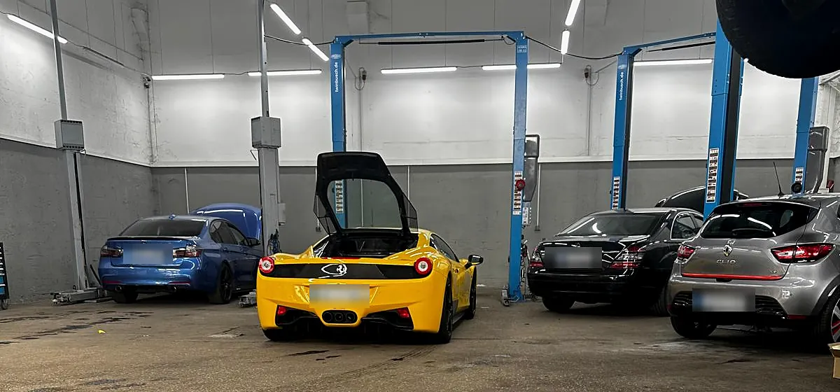 Gelber Ferrari 458 mit geöffneter Tür neben einem blauen BMW M in der Werkstatthalle