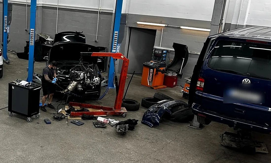 Mechaniker arbeitet mit einem Motorkran an einem ausgebauten Motor in der Werkstatthalle